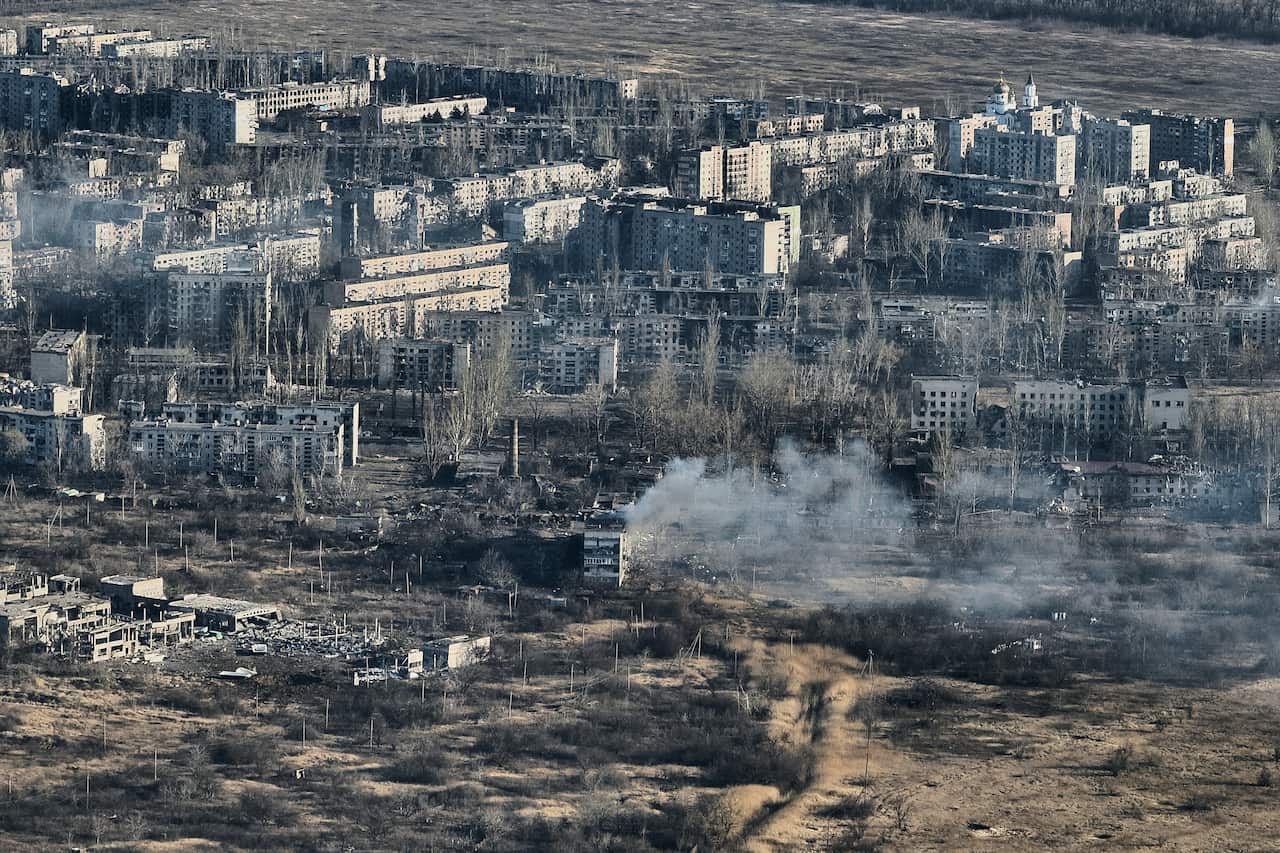 An aerial view of heavily damaged buildings. Smoke rises from some of them.