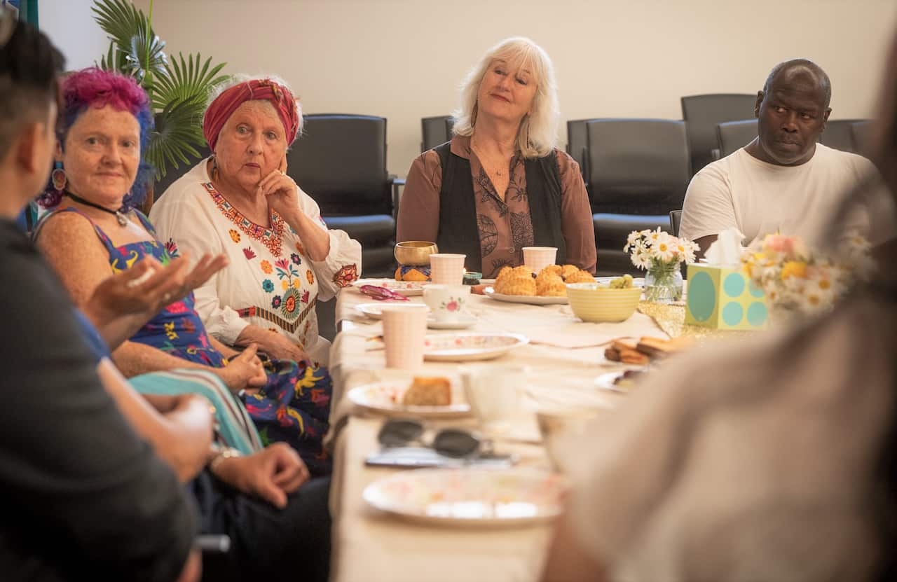 A group of people sitting around a table with tea and cakes.