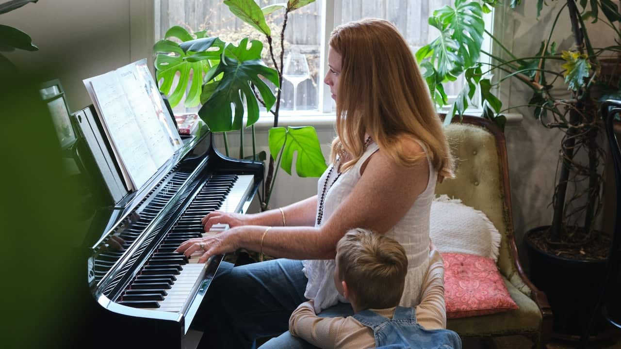 a young woman with red hair plays the piano while a young child hugs her lap