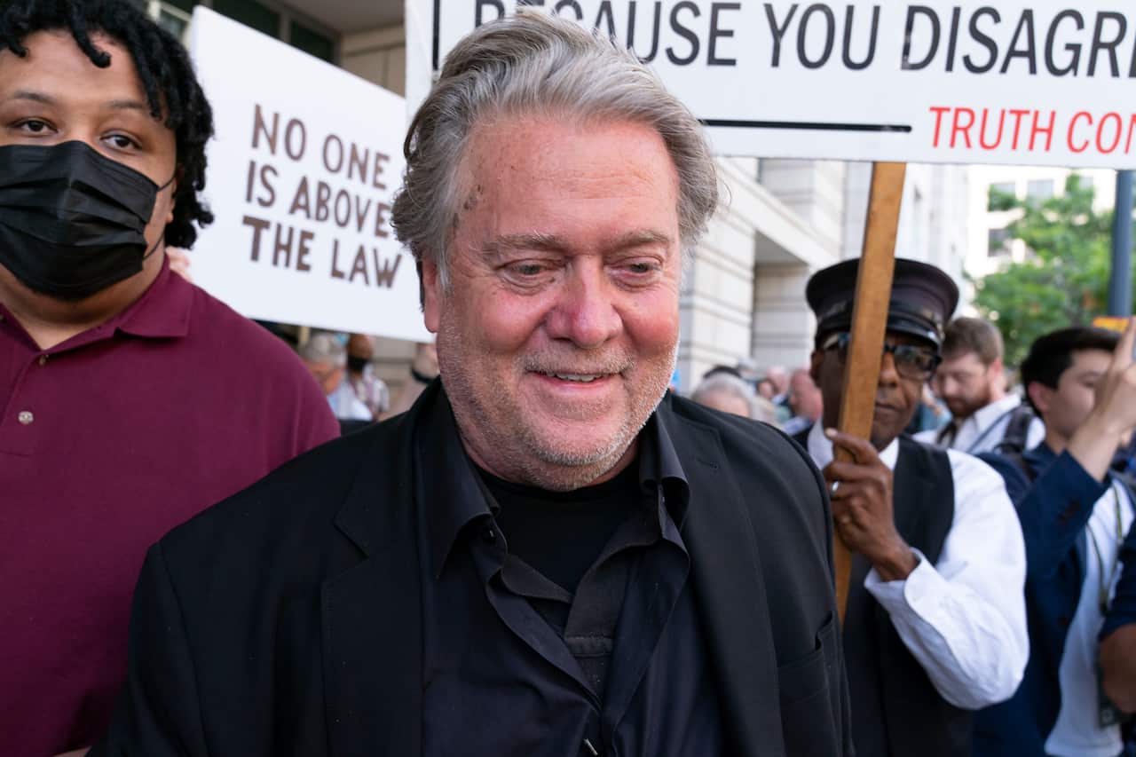 Steve Bannon smiles in front of a sign that says: "no one is above the law". 