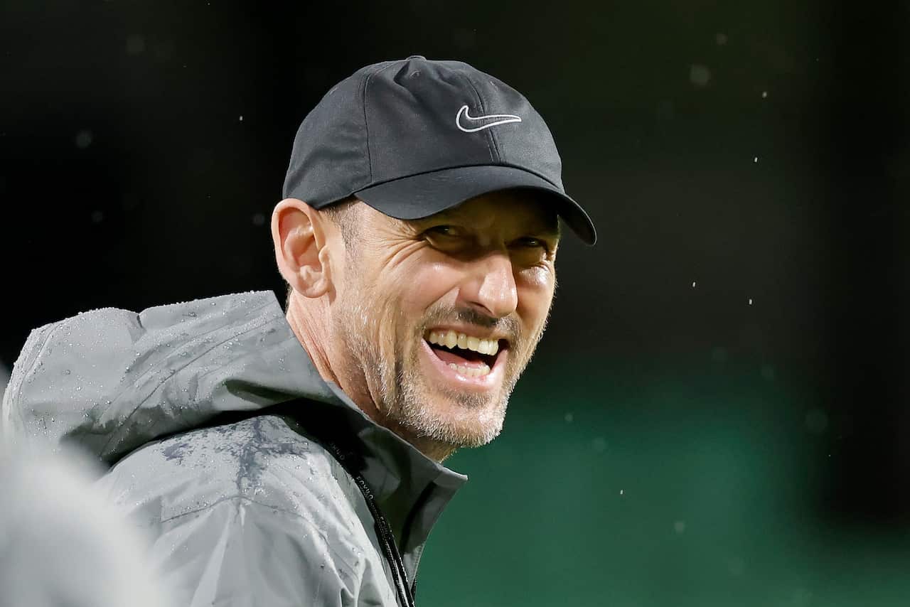 A man wearing a black jacket and cap is smiling.