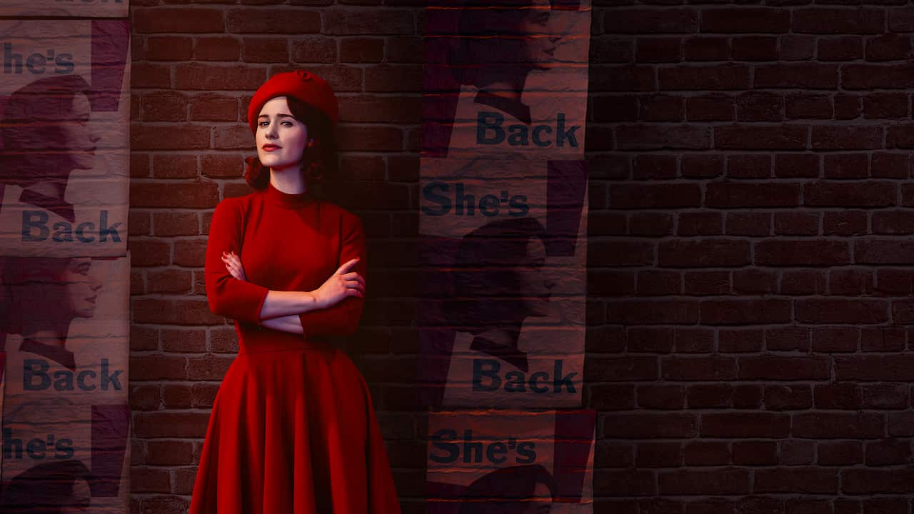 A woman in a 1950s red dress and beret stands in front of a brick wall with her arms crossed and a smile on her face