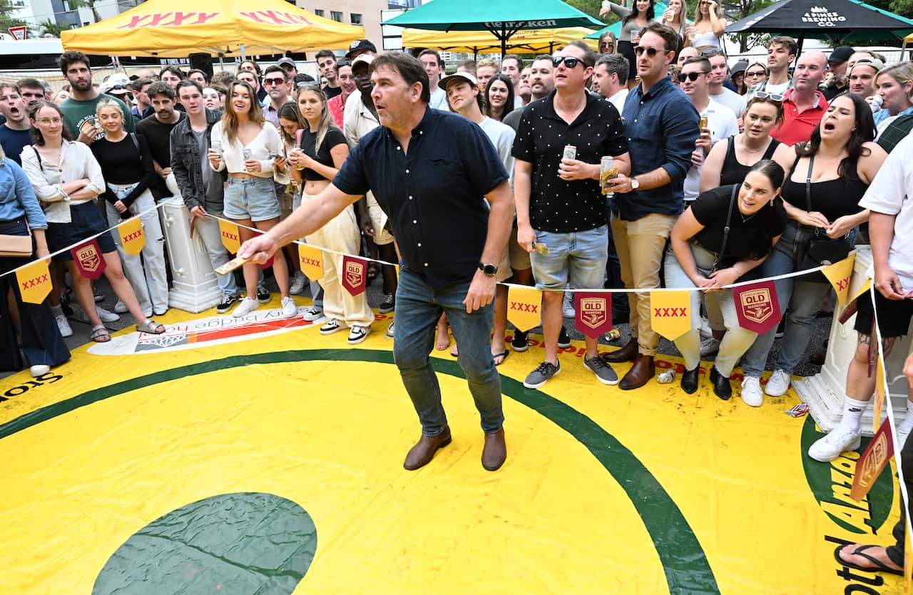 A man plays a game of two-up while a large crowd watches.
