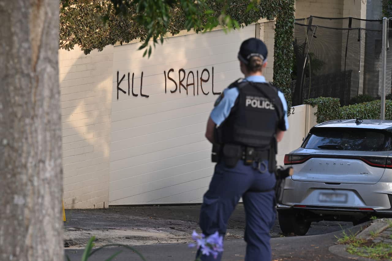 A police office looking at a wall that has been graffitied with the worlds "Kill Israiel (sic.)"