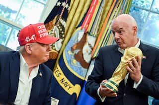 Donald Trump, wearing a red cap reading "Trump was right about everything" sits next to Gianni Infantino, who is standing and holding a gold trophy