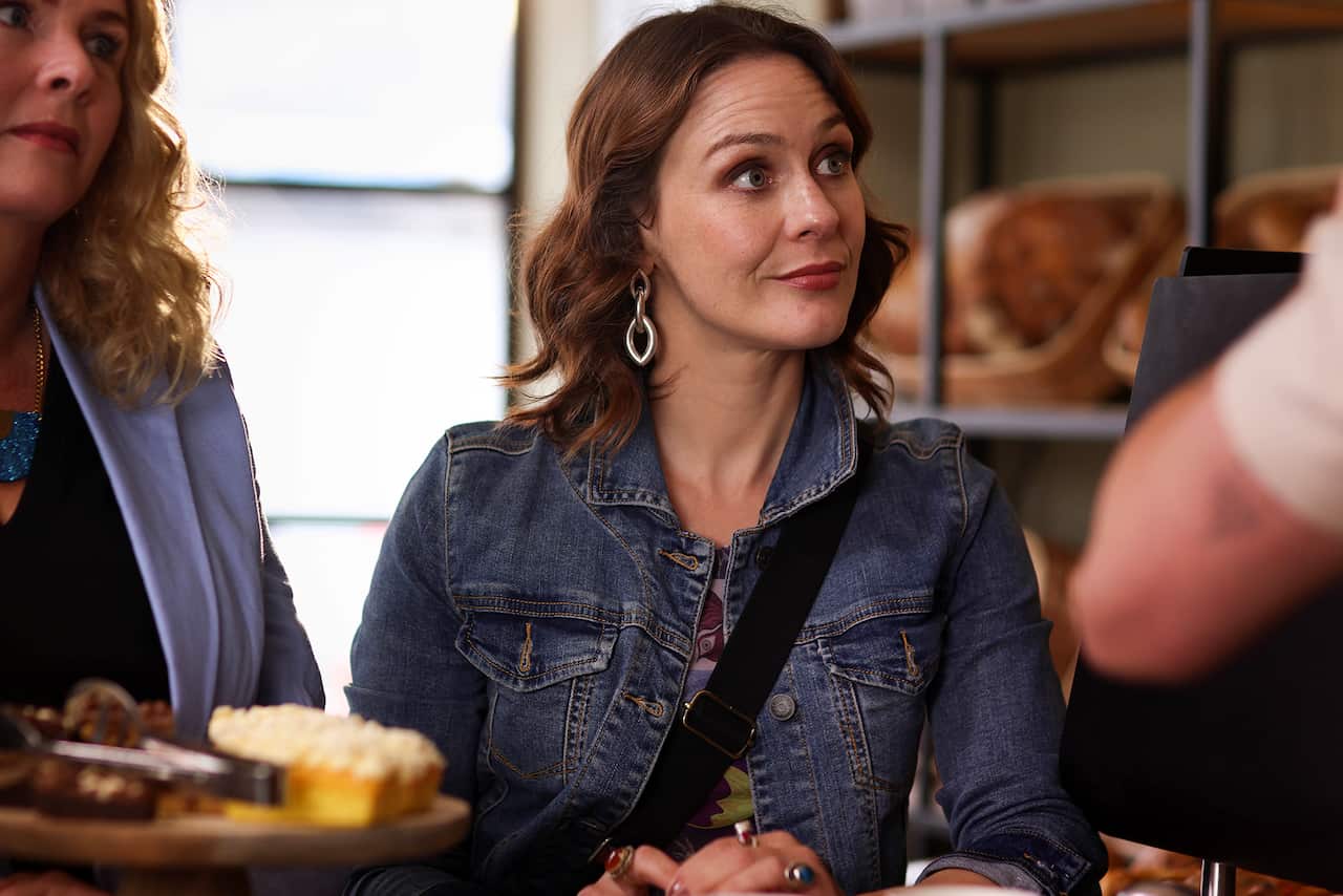 A woman in a denim jacket smiles at someone out of the frame. 