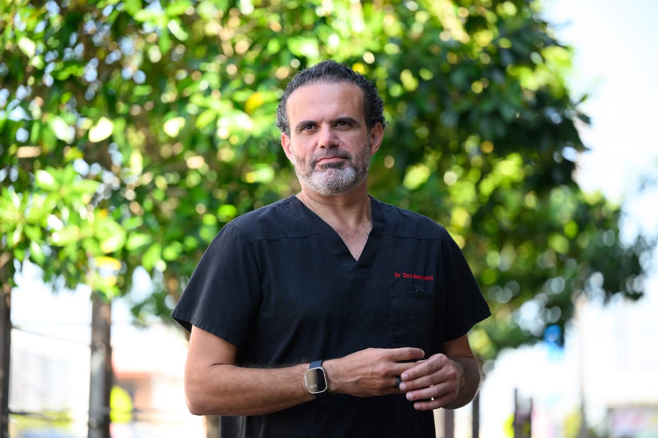 A man in dark scrubs standing in front of a tree