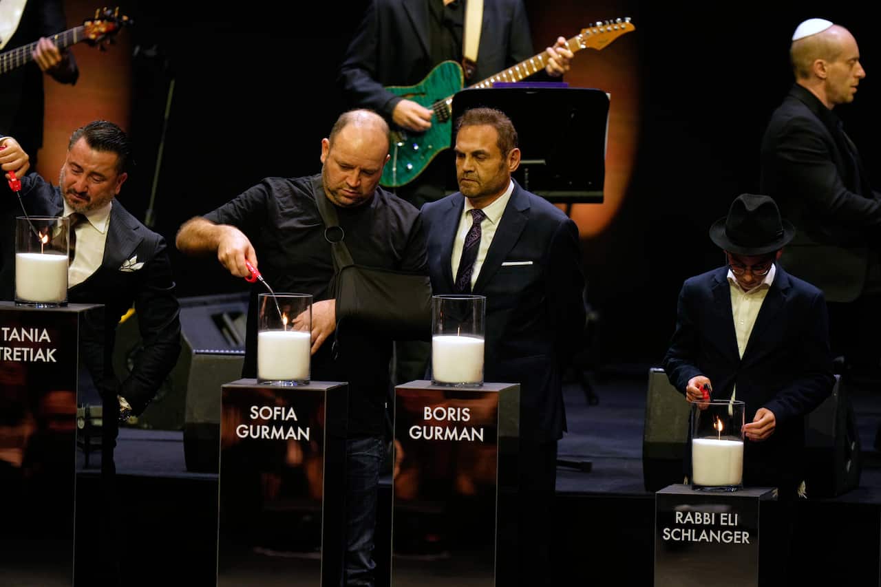Several people light candles on a stage. Each candle is labelled with a name.