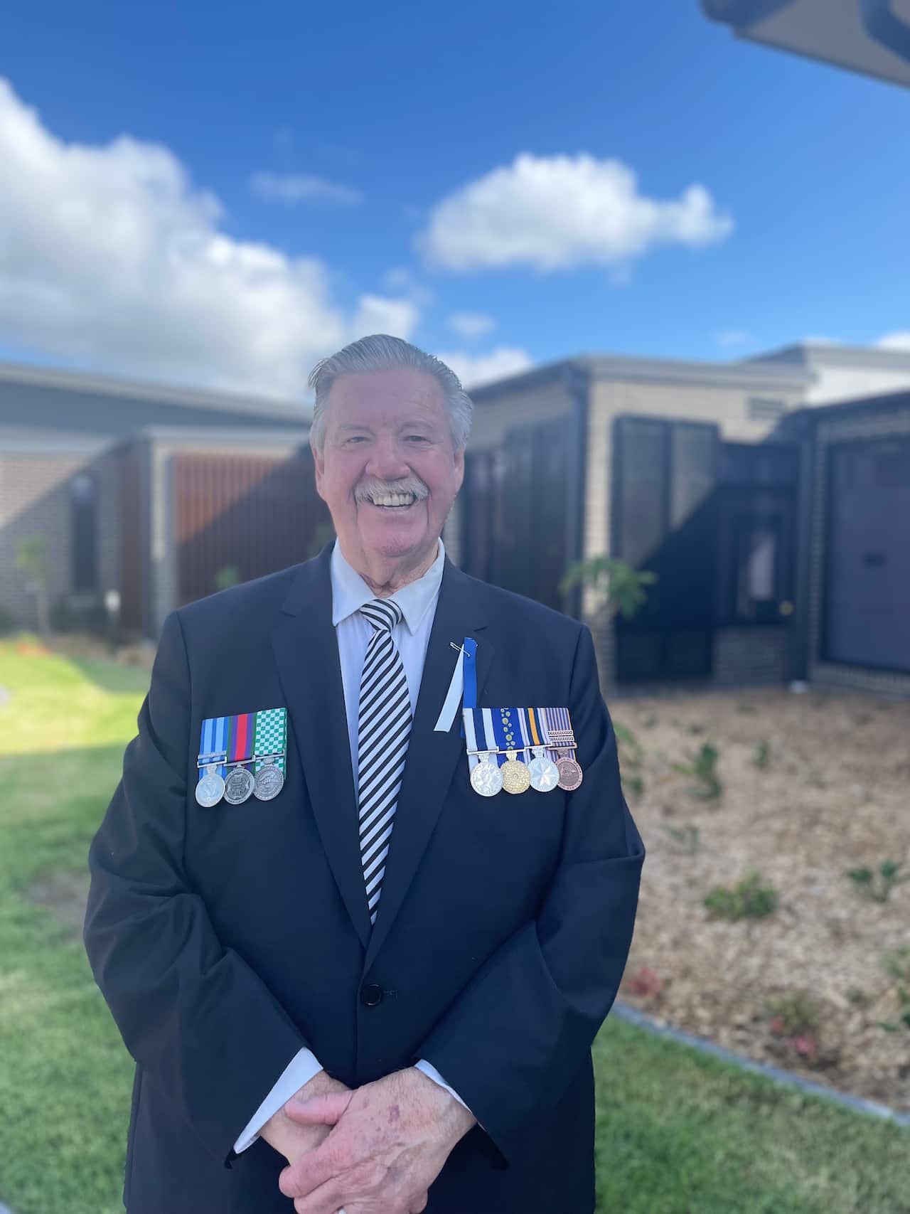 A man standing outside in a suit with medals on each side of his chest. 