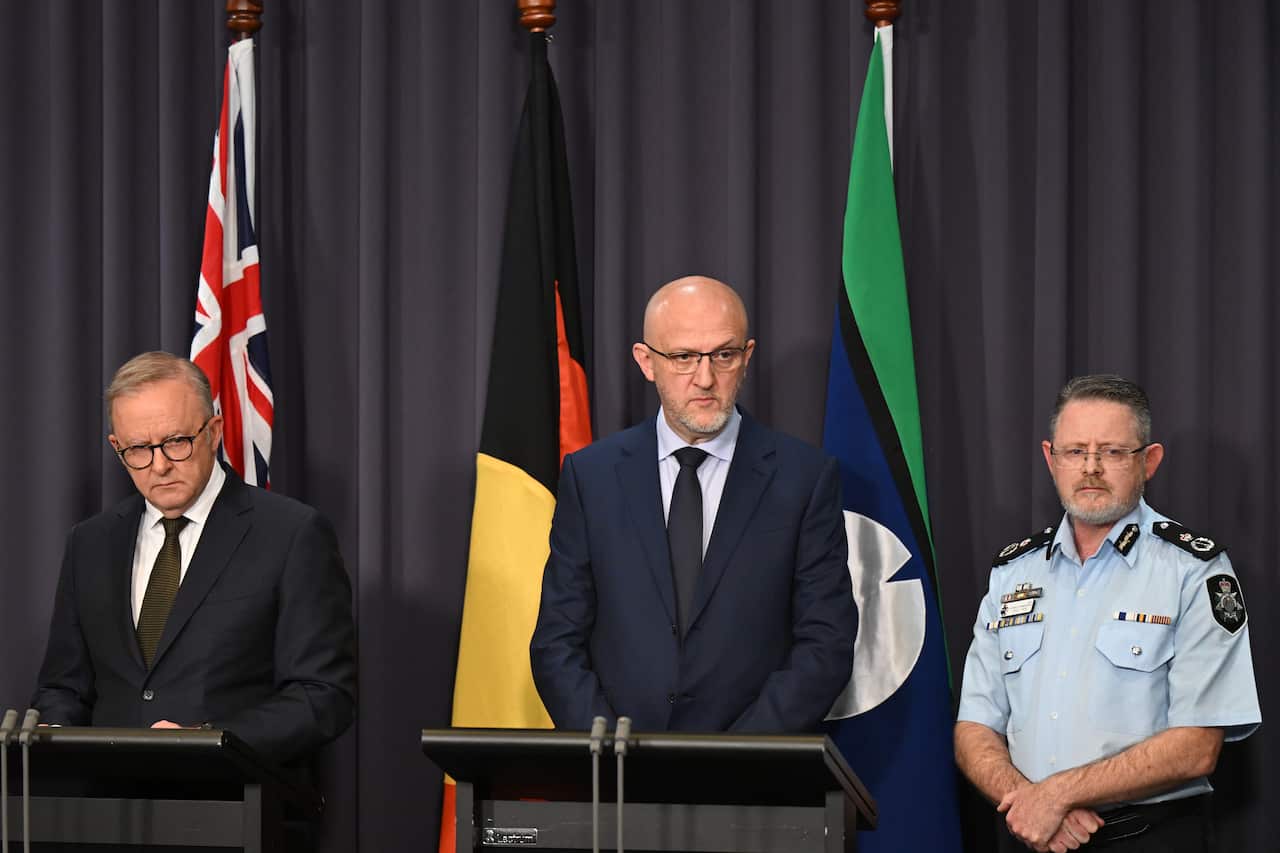 Two men stand at lecterns while a police officer stands nearby.