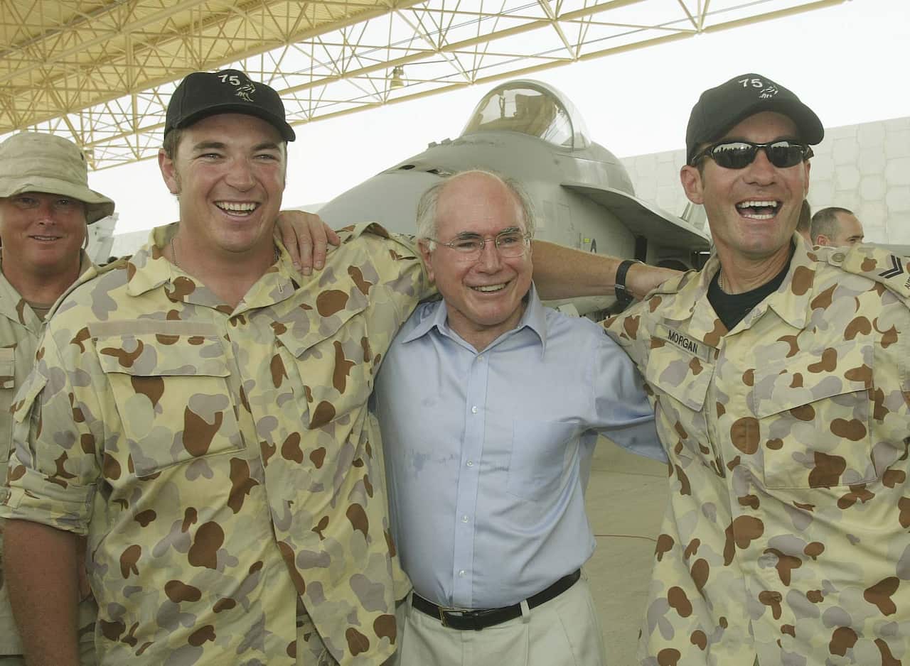 Two men in army camouflage shirts put their arms around an elderly man in a white shirt.