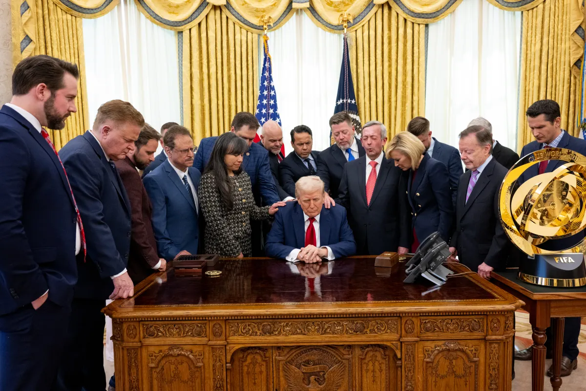 A group of people pray while holding one hand in a circle on Donald Trump's shoulder