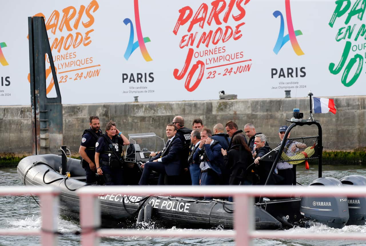 Emmanuel Macron on a boat with security officers and others in suits on the River Seine.