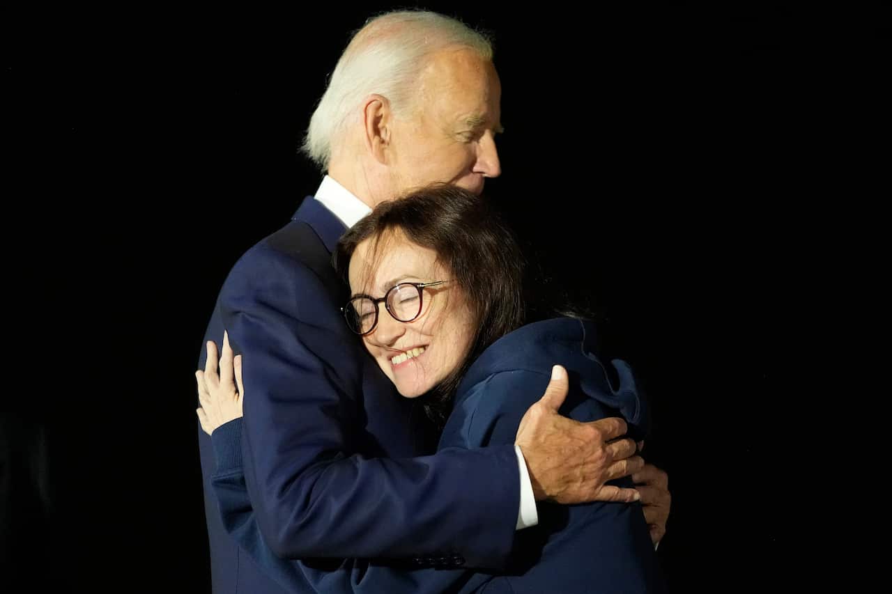 President Joe Biden hugs a young woman wearing glasses with long dark hair. 