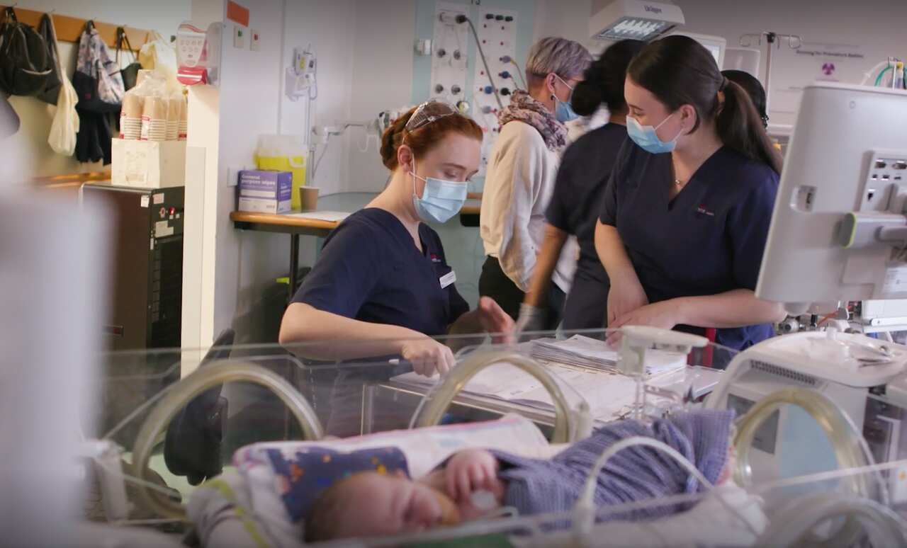 A baby in a hospital surrounded by staff.