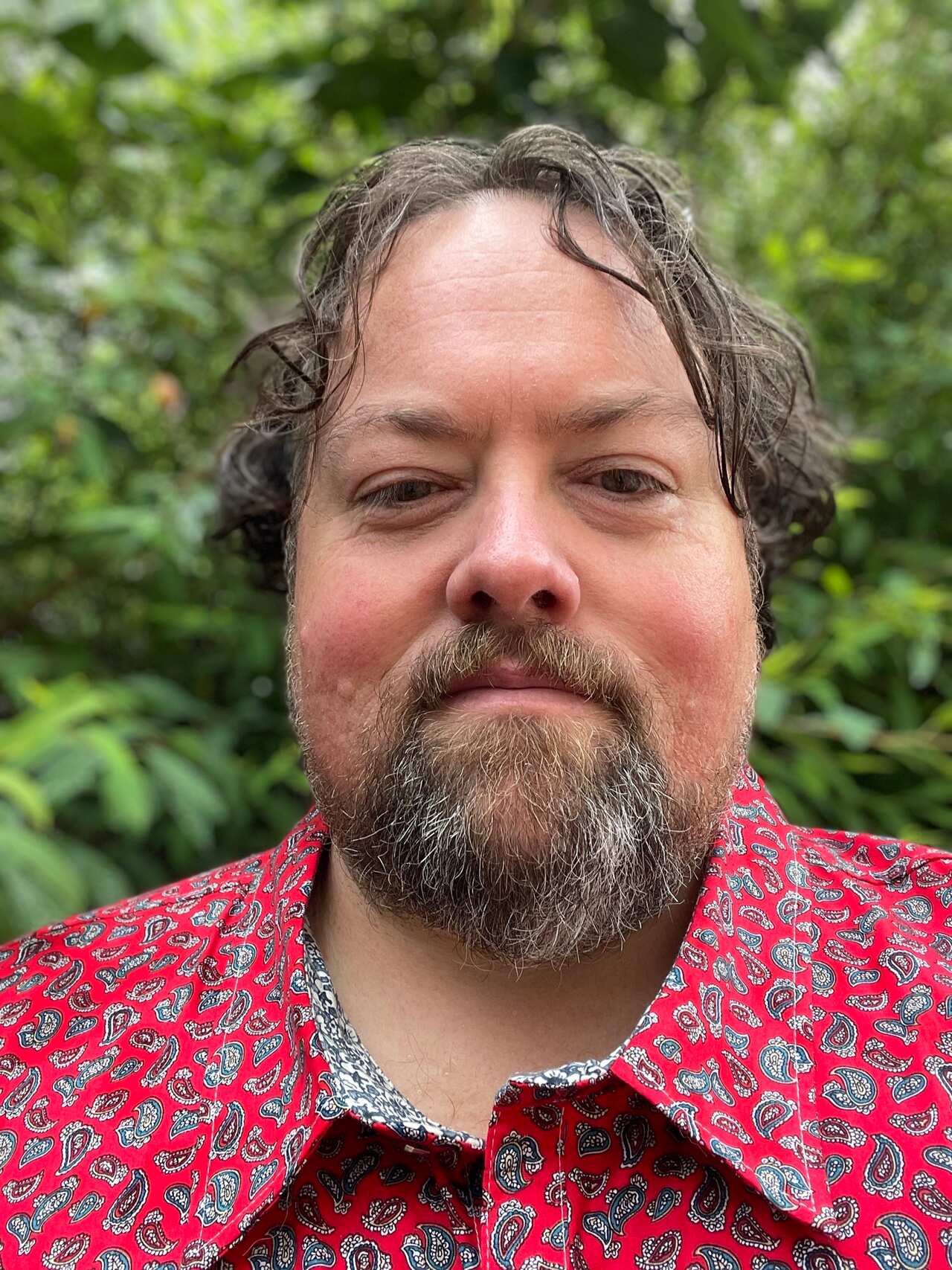 A man wearing a red patterned collared shirt 