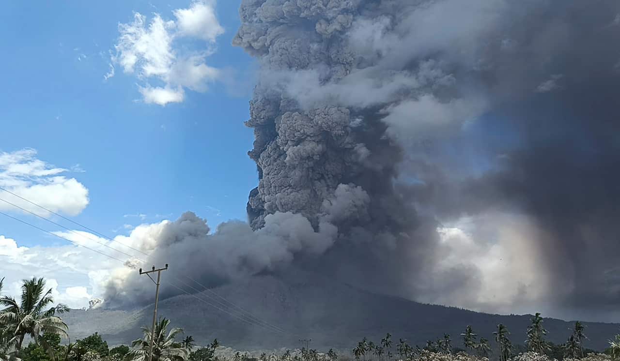 Ash rising from a volcanic eruption, with mountains in the distance.