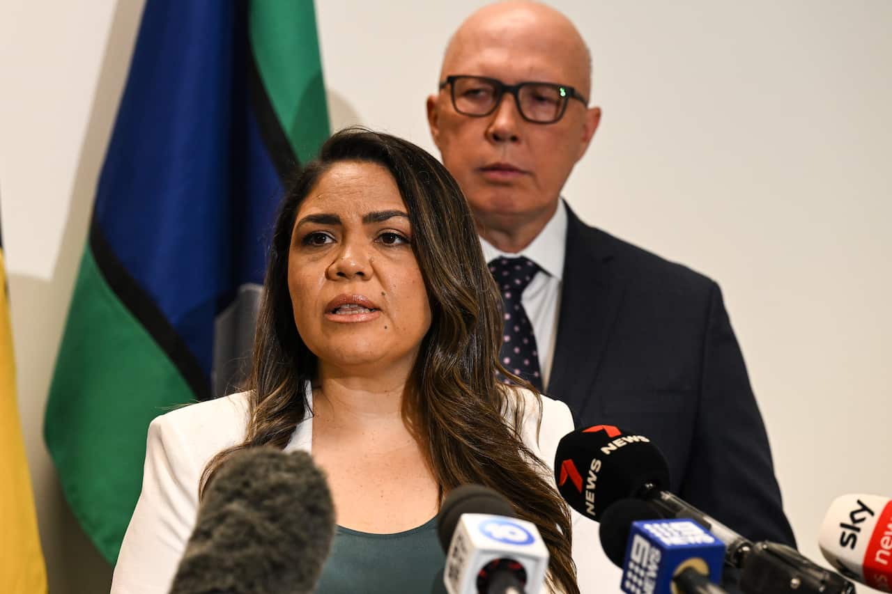 A woman speaking in front of mikes with Opposition leader Peter Dutton standing in the background.