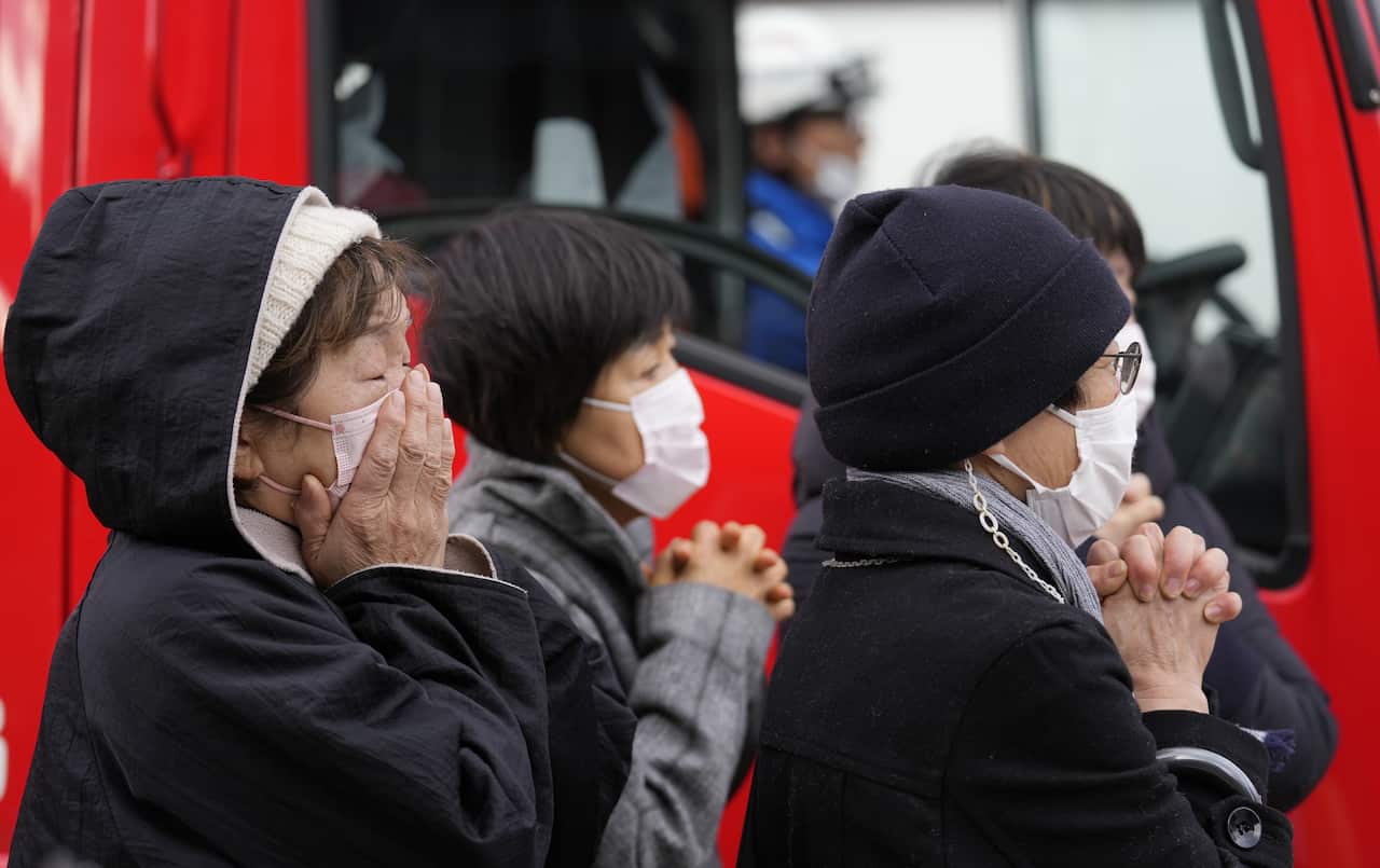 A group of people in winterwear and face masks clasp their hands.