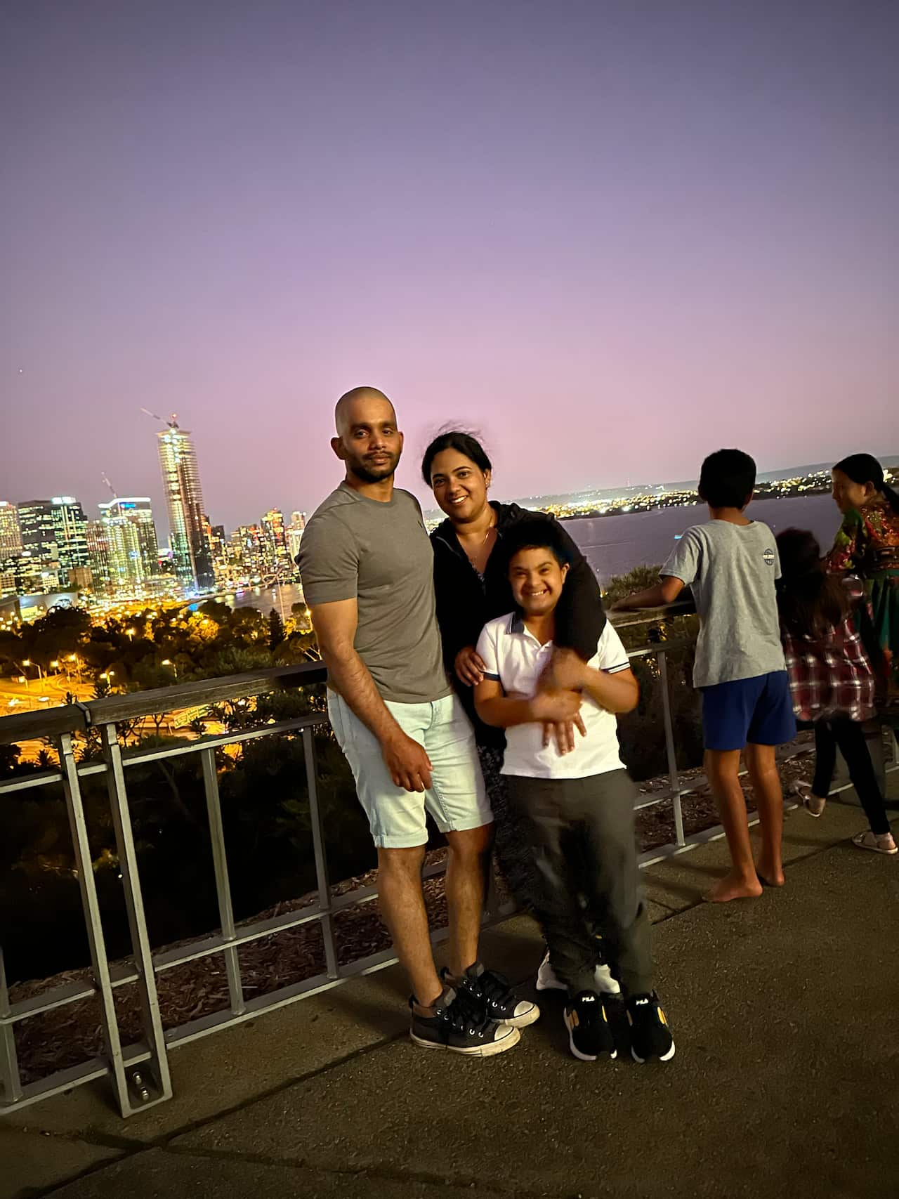 Two adults and their son smile in front of a cityscape.