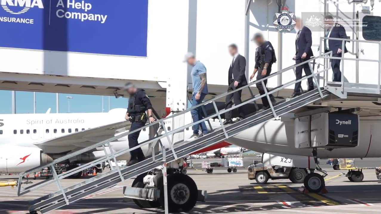 Police escorting a man down a ramp from an aerobridge to the tarmac.
