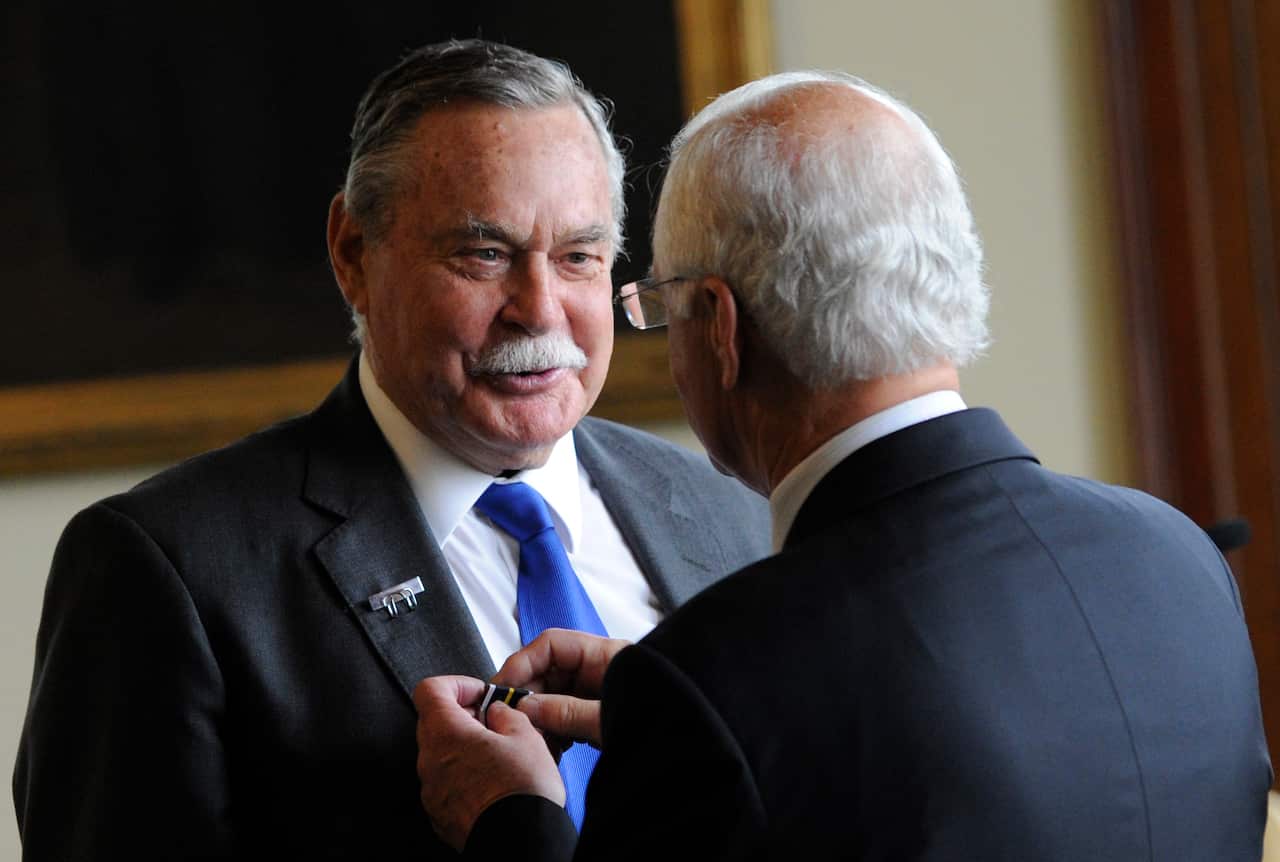 A man in a suit having a medal pinned on him by another man.