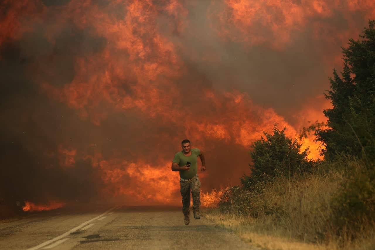 A man runs away from a wildfire on a road.