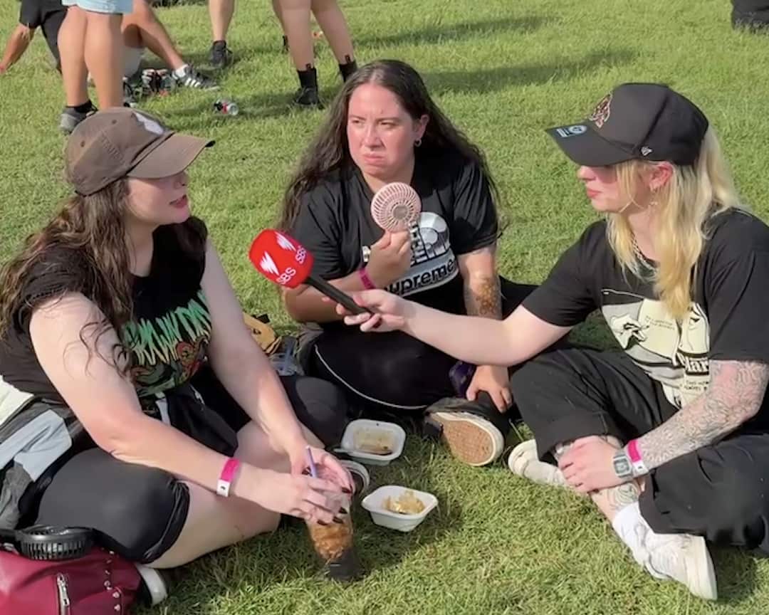 A woman wearing an all-black outfit interviews two festivalgoers.