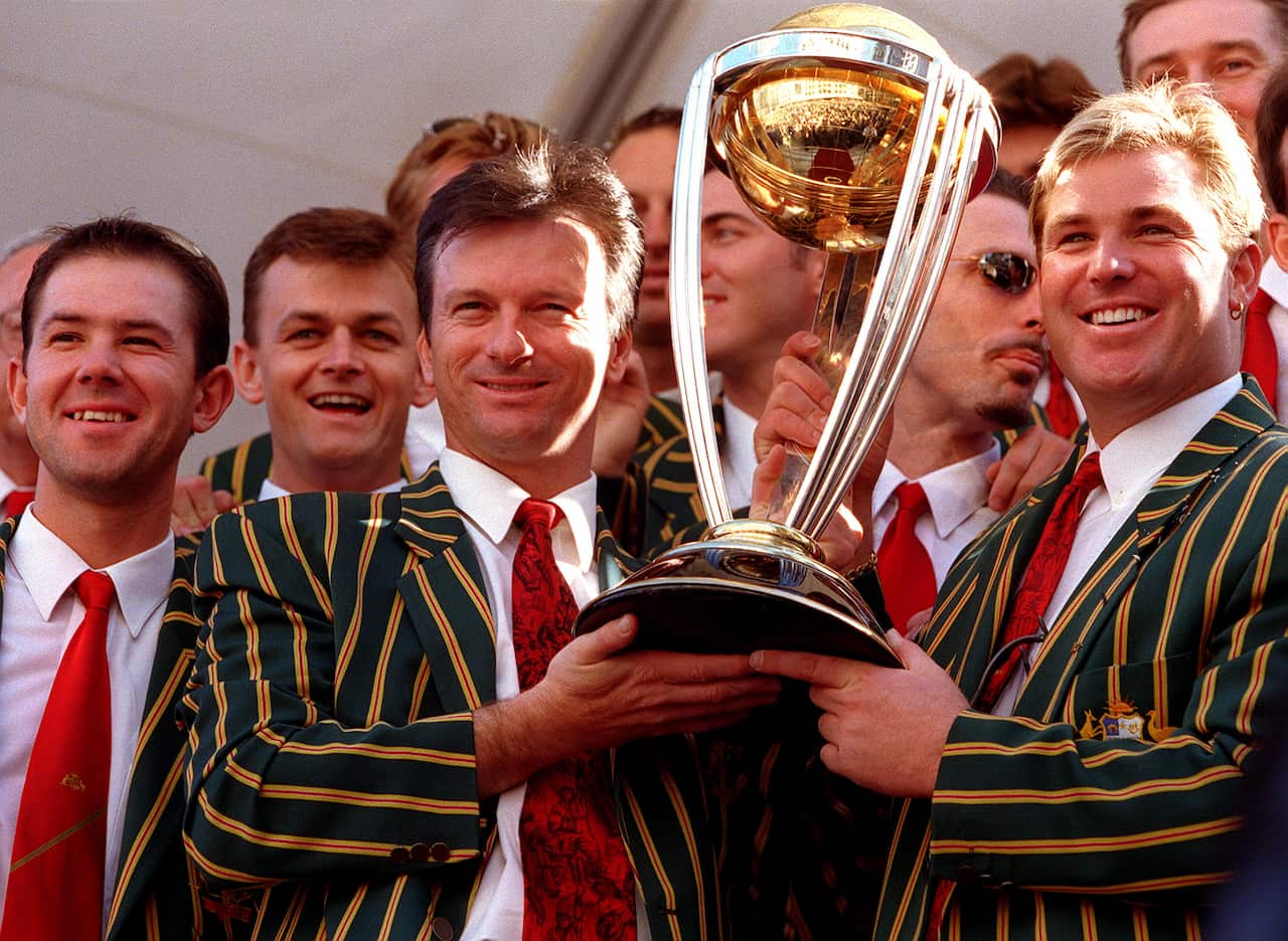 Steve Waugh and Shane Warne are seen smiling while holding the World Cup trophy.