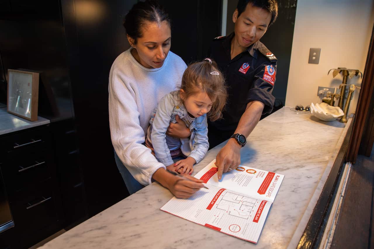 A firefighter points to a booklet next to a woman holding a toddler