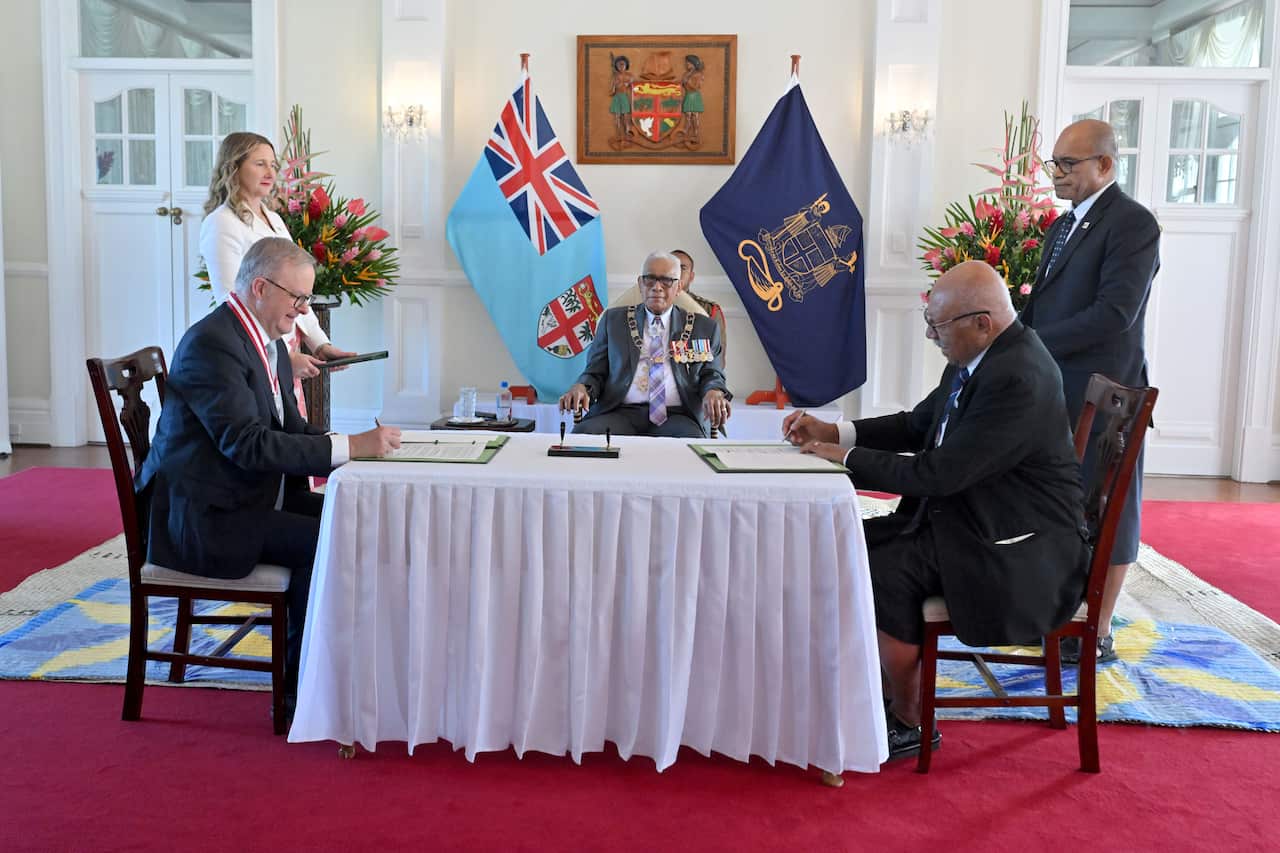 Anthony Albanese sits at a table in a decorated room signing documents