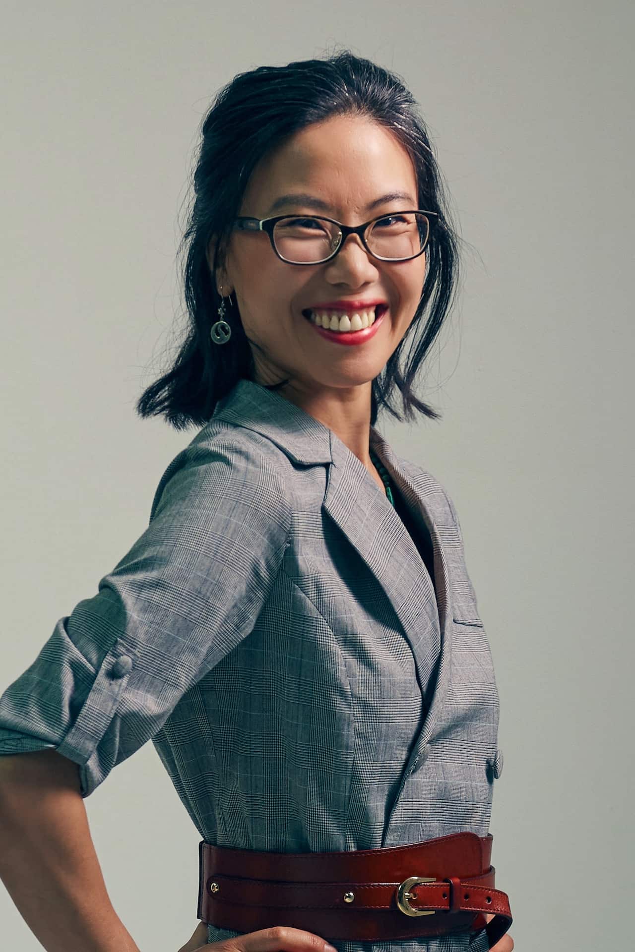 An Asian woman smiles as she poses with her hands on her hips 