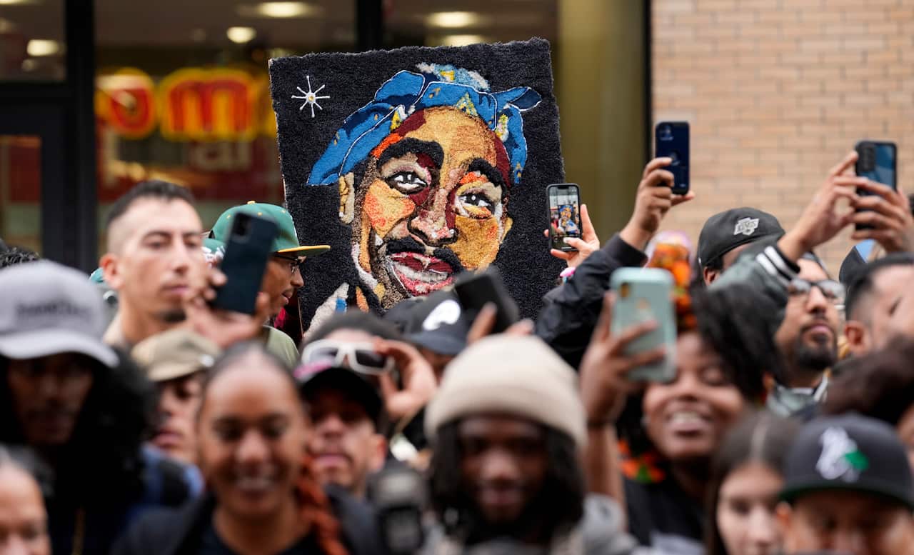 A crowd of fans clicking pictures with their mobile phones, with a person holding a colourful sketch of late US rapper Tupac Shakur behind them.