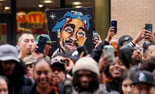 A crowd of fans clicking pictures with their mobile phones, with a person holding a colourful sketch of late US rapper Tupac Shakur behind them.
