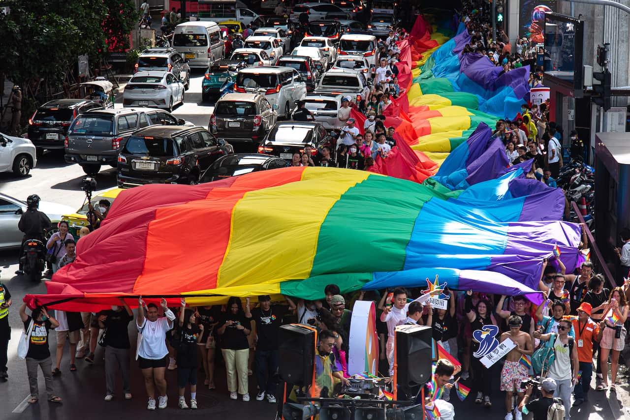 Participants march on Sukhumvit road while holding a rainbow