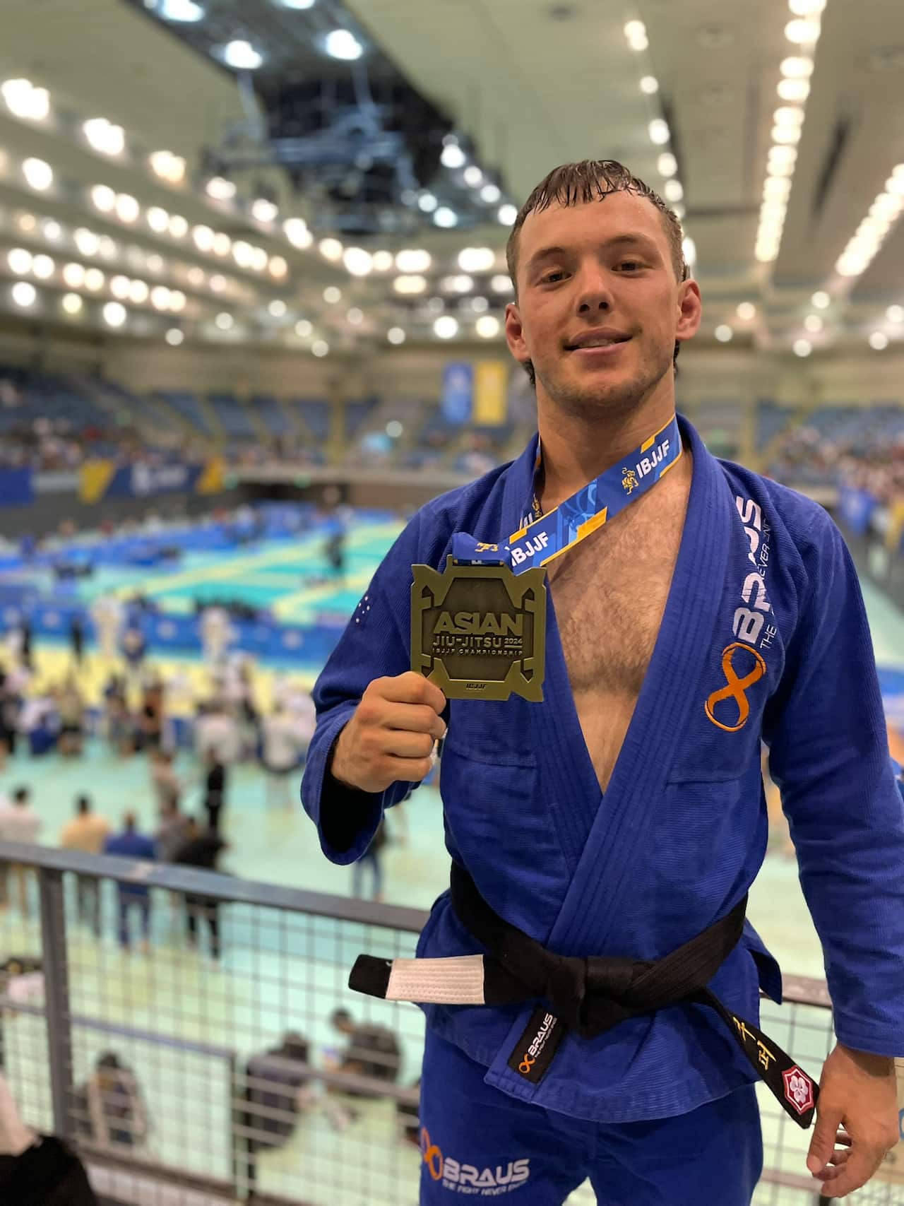 A man wearing a blue martial arts uniform shows a medal.