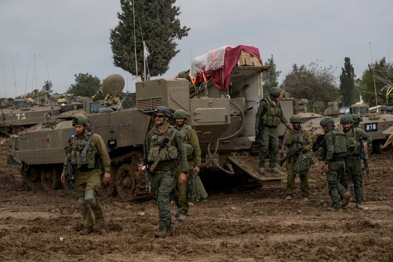 Soldiers standing near tanks which are parked on a muddy road.