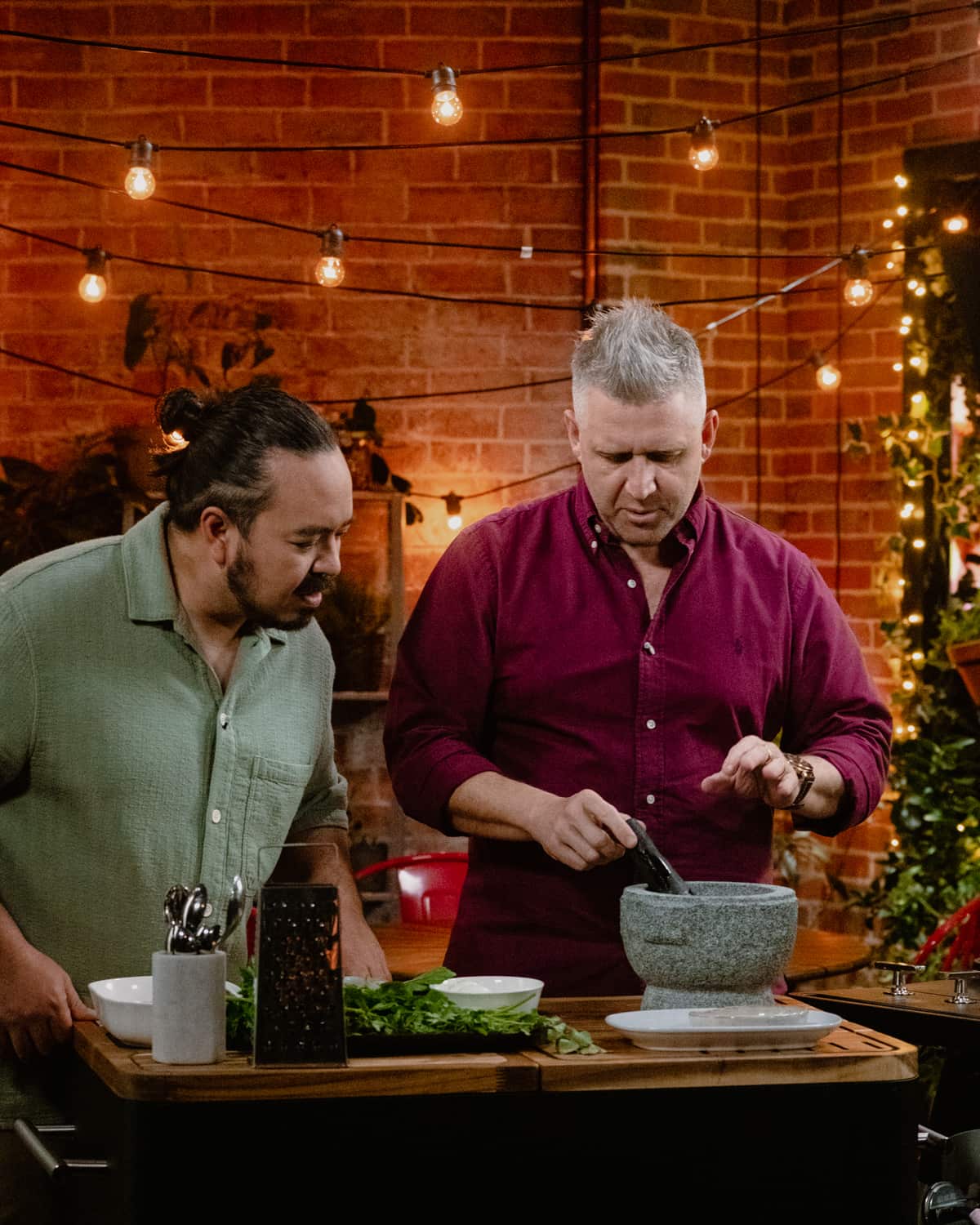 Massimo Mele uses a mortar and pestle (left) on a cooking bench while Adam Liaw observes in a kitchen.