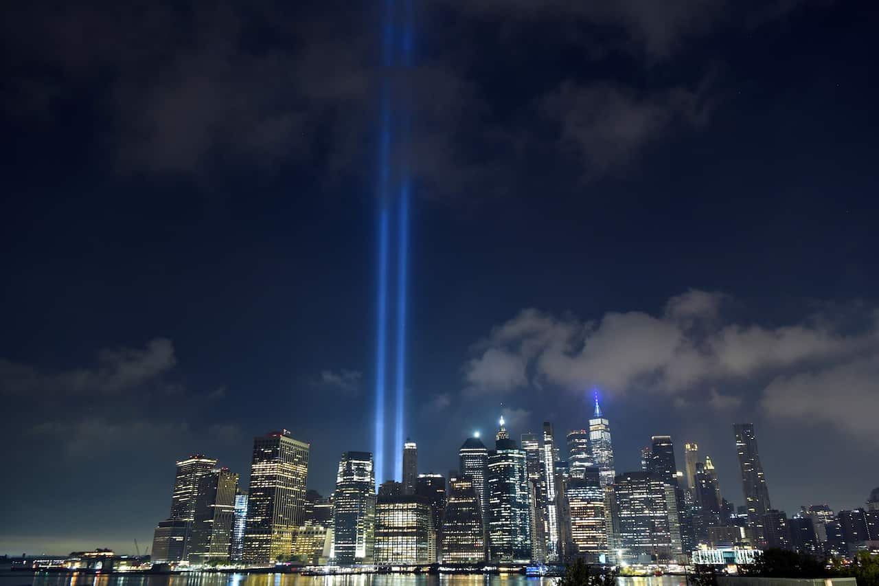 Two large searchlights stretch into the sky amid the lights of numerous high rise towers. 