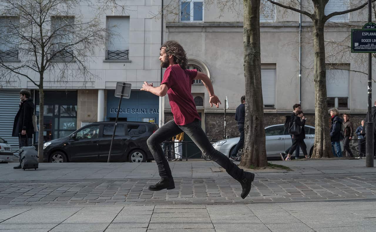 A bearded man runs along a street, as if being chased.