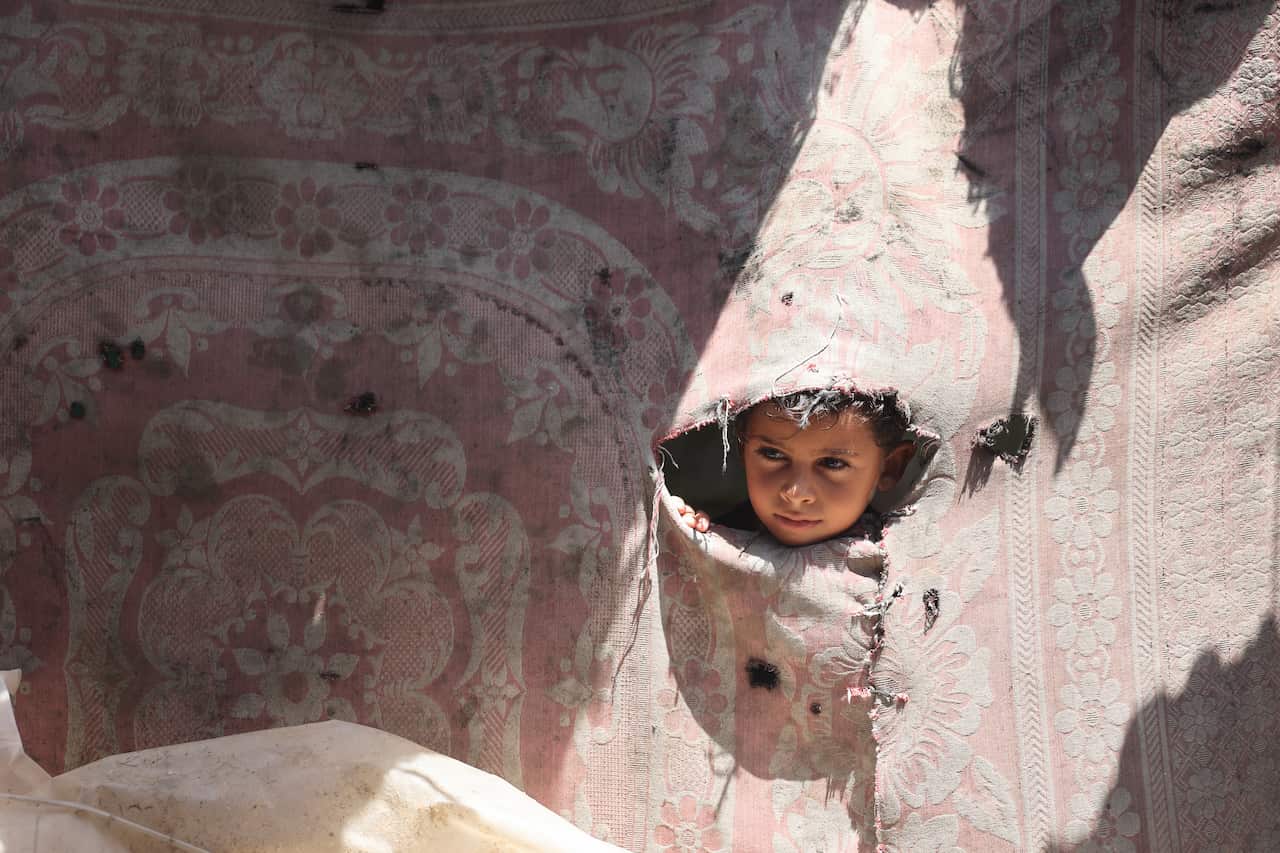 A child looks through a hole in a rug