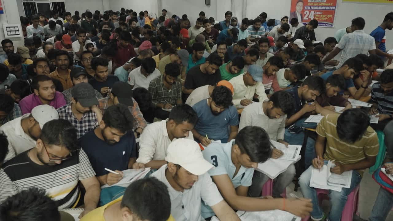 A crowded classroom of young men writing in their notebooks with their heads down