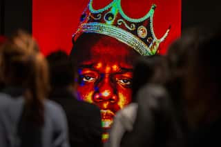 A crowd is looking at a photograph of US rapper Biggie Smalls wearing a crown. It's a close-up of the rapper's face taken against a red backdrop.