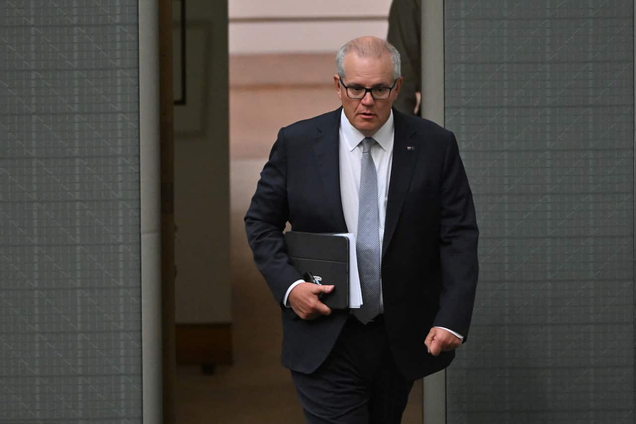 Former prime minister Scott Morrison walks into the House of Representatives at Parliament House in Canberra. He is carrying an iPad and a pile of papers. 