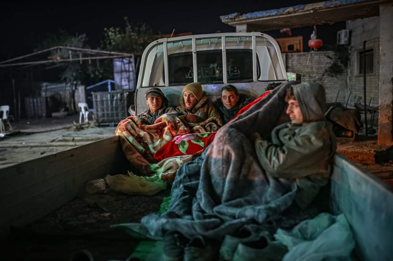 Men huddled in blankets on the tray of a utility vehicle.