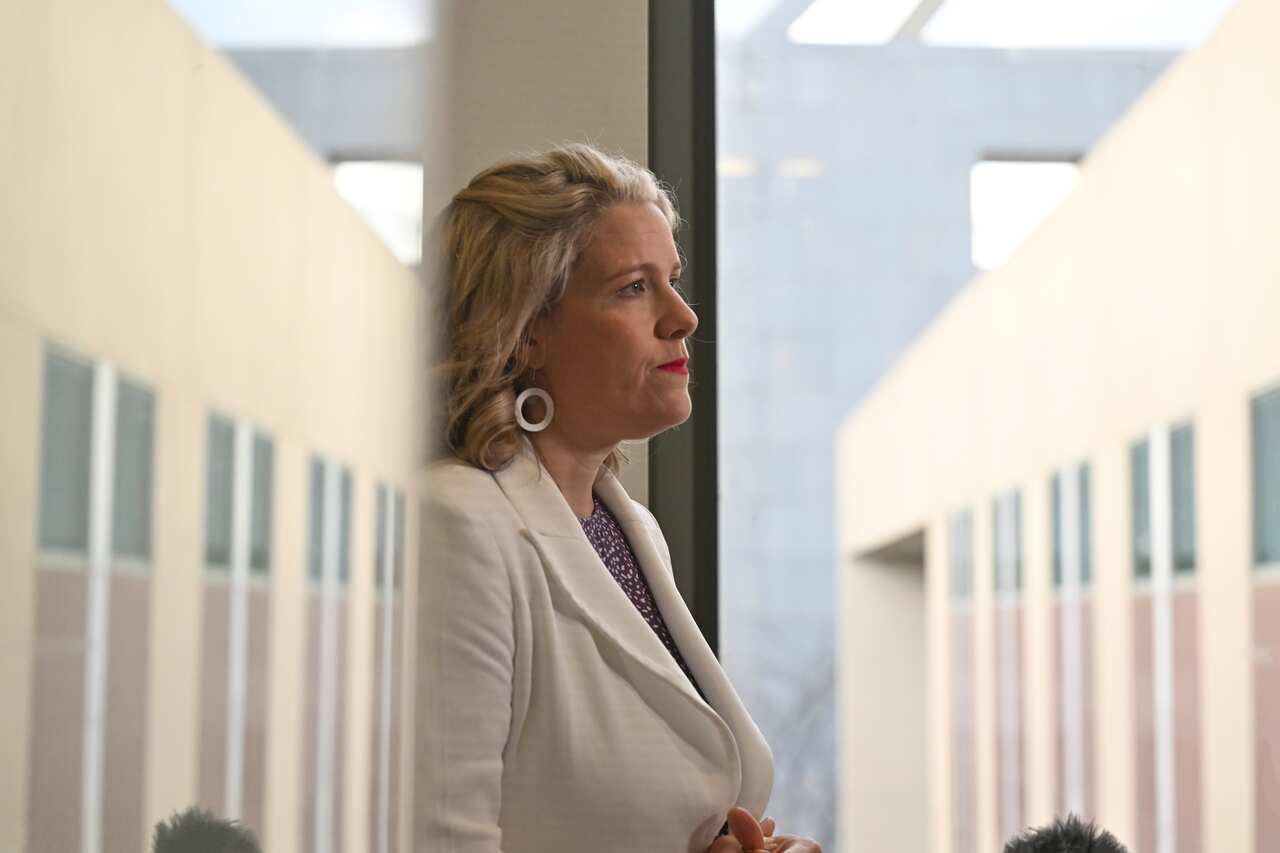 Woman in blazer walks through a corridor, with parliament house reflected back.