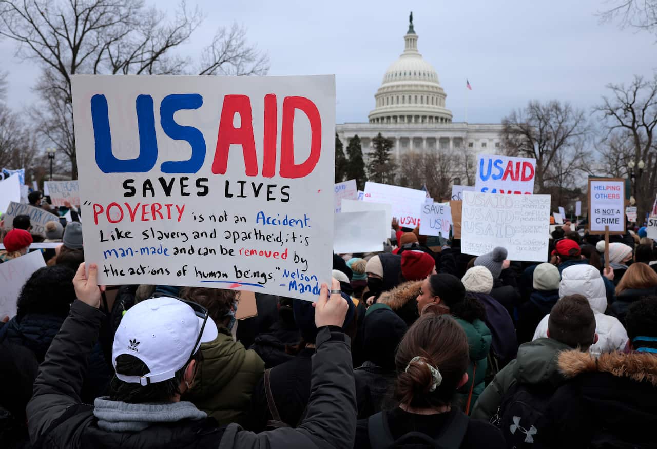 A crowd of protesters holding placards reading "USAID Saves Lives" in front of the US Capitol in Washington DC.