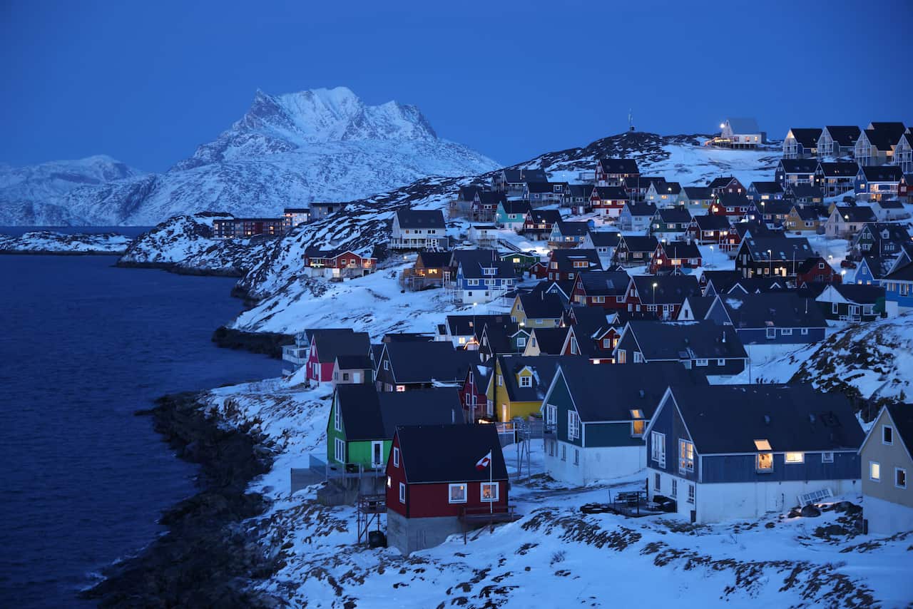 Houses on a snowy landscape at dusk, next to water