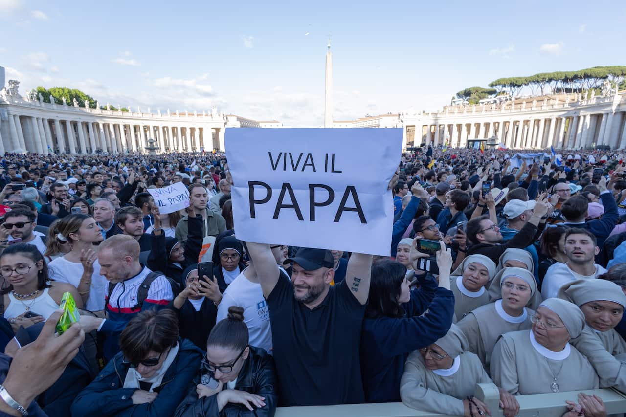 A man holds up a sheet of paper reading 'Viva il Papa' in front of a large crowd.