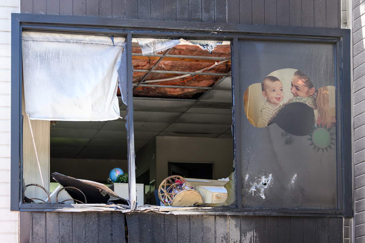 A shattered glass window in a fire-ravaged building, with one part covered by a poster of a woman smiling at a child.